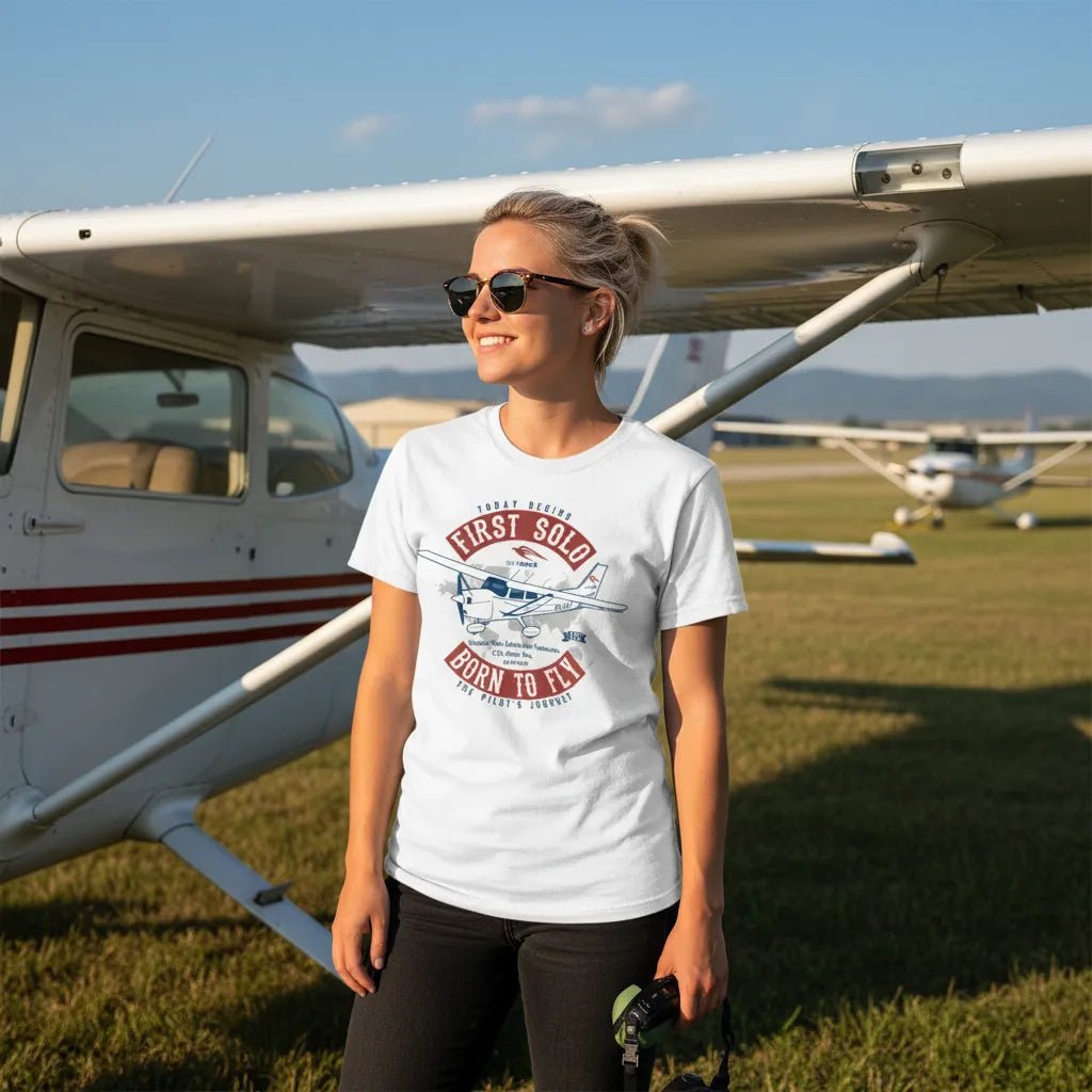 Woman wearing a white personalized First Solo T-shirt beside a high-wing airplane on an airfield