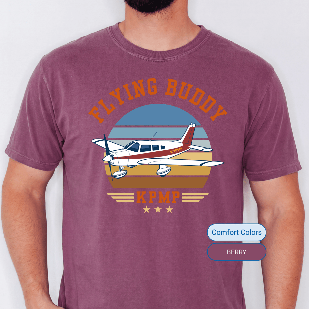 Man wearing a Berry Comfort Colors Flying Buddy T-shirt with a red-and-white airplane and KPMP airport code
