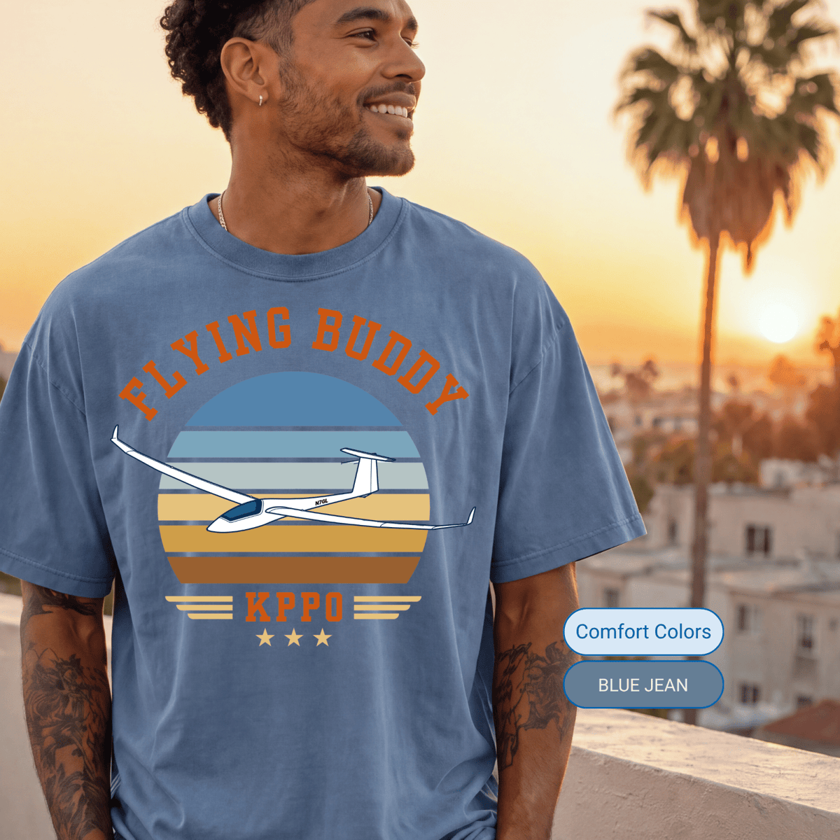 Man wearing a Blue Jean Comfort Colors Flying Buddy T-shirt with a glider at sunset