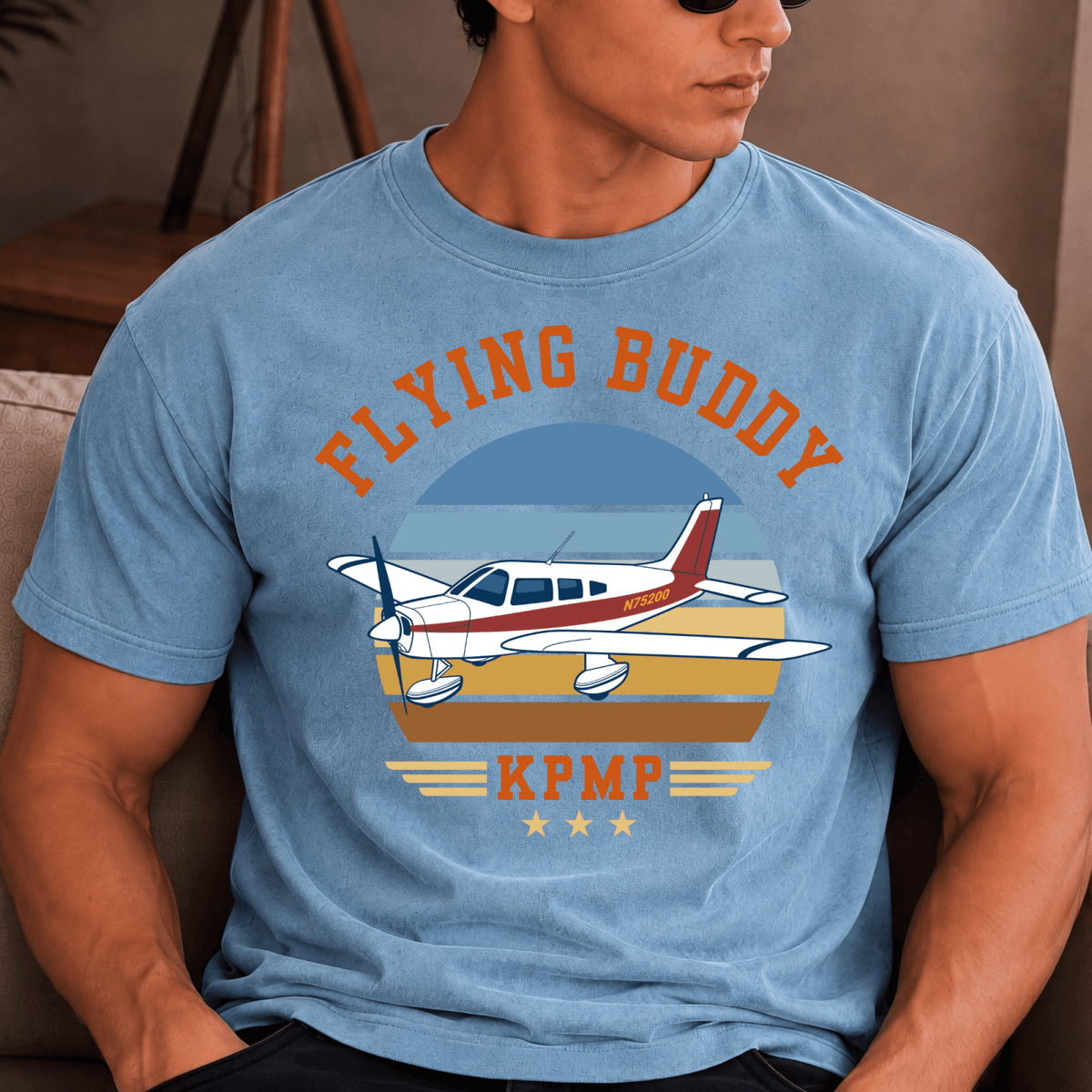 Man wearing a blue Flying Buddy T-shirt with a red-and-white airplane and KPMP airport code
