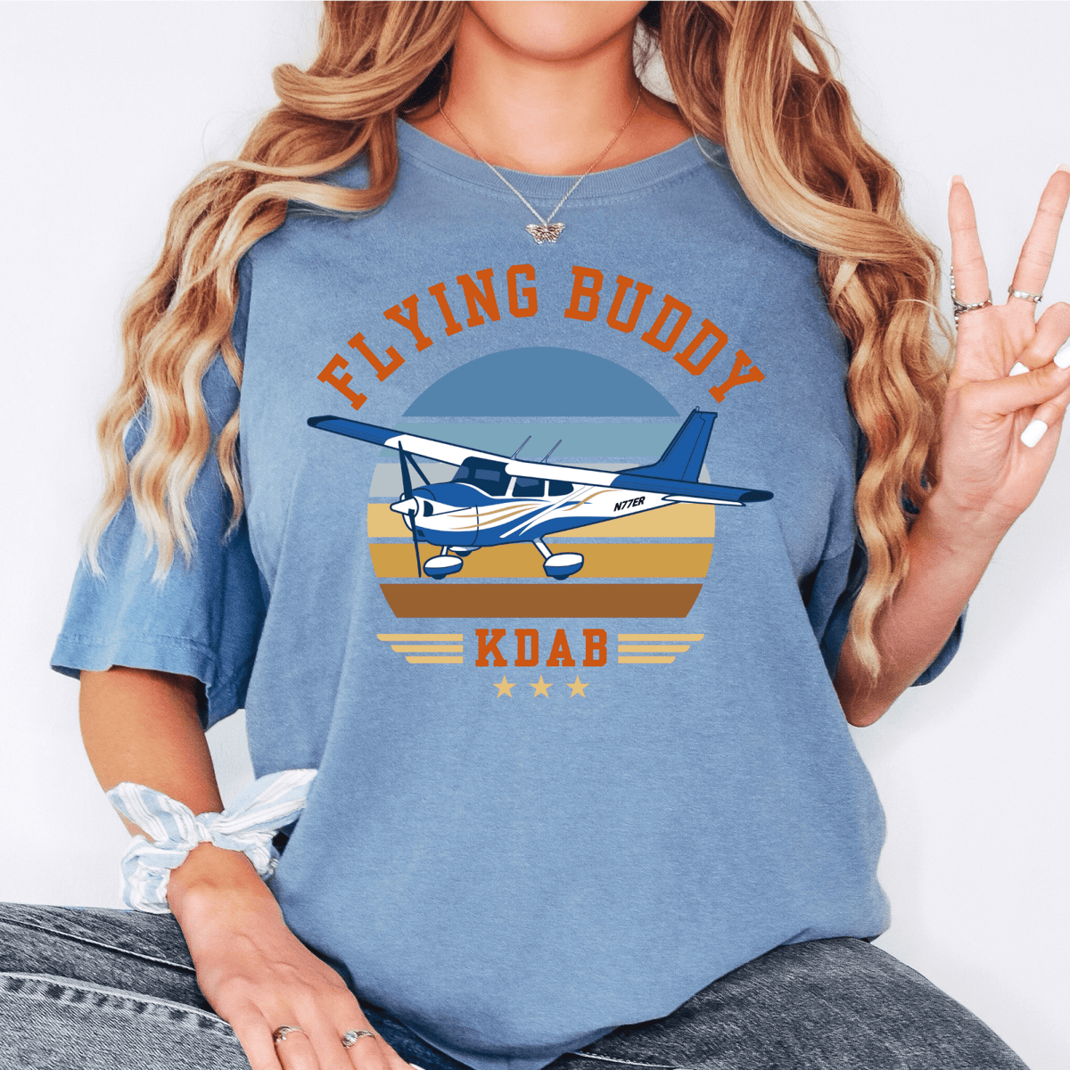 Woman wearing a blue Flying Buddy T-shirt with a blue-and-white airplane and KDAB airport code