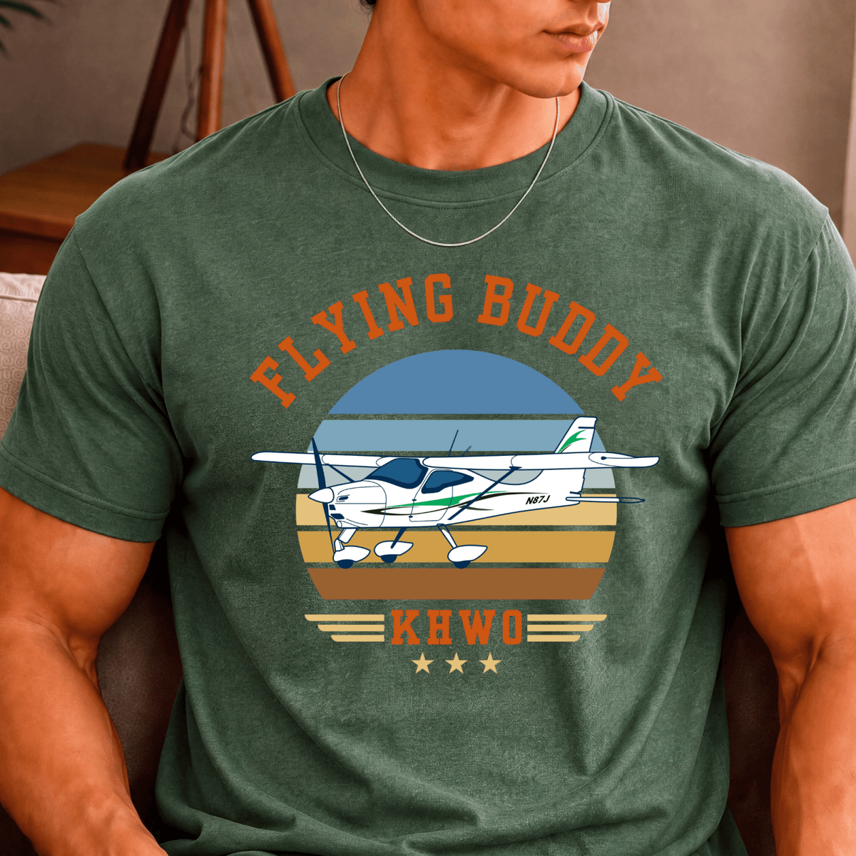 Man wearing a green Flying Buddy T-shirt with a high-wing airplane, retro striped background, and KHWO airport code