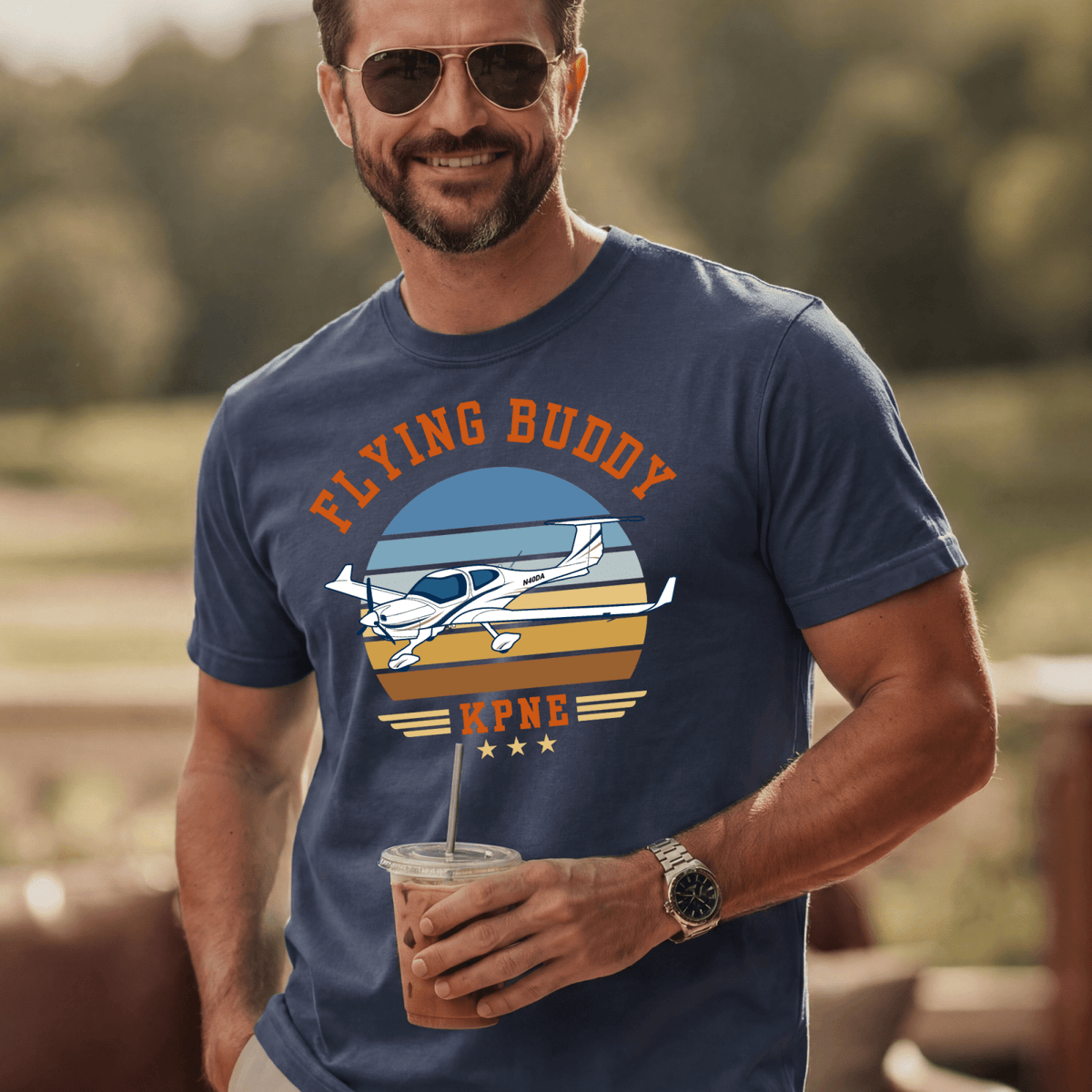 Man wearing a navy Flying Buddy T-shirt with an airplane and KPNE airport code outdoors