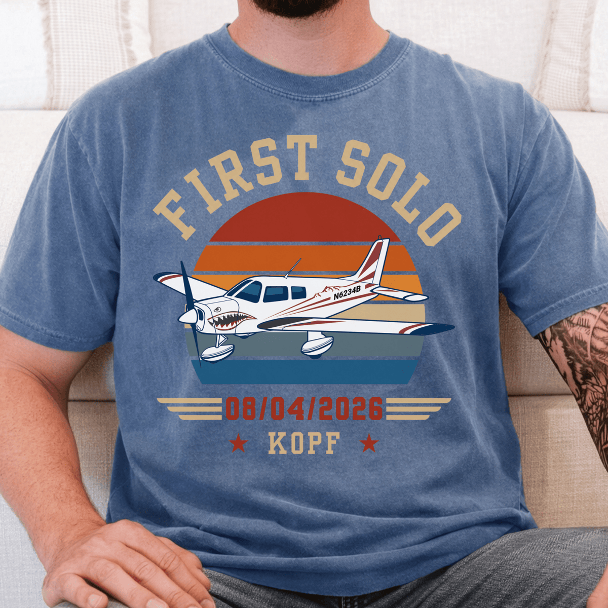 Blue First Solo T-shirt with a low-wing airplane illustration, striped sunset, flight date, and airport code