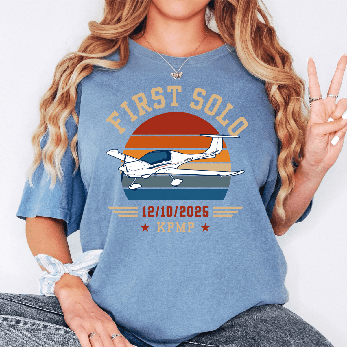 Woman wearing a blue First Solo T-shirt with a white airplane, striped sunset, and personalized date