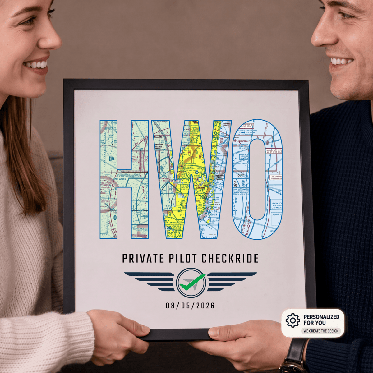 Couple holding a black-framed HWO airport code print personalized with a private pilot checkride date