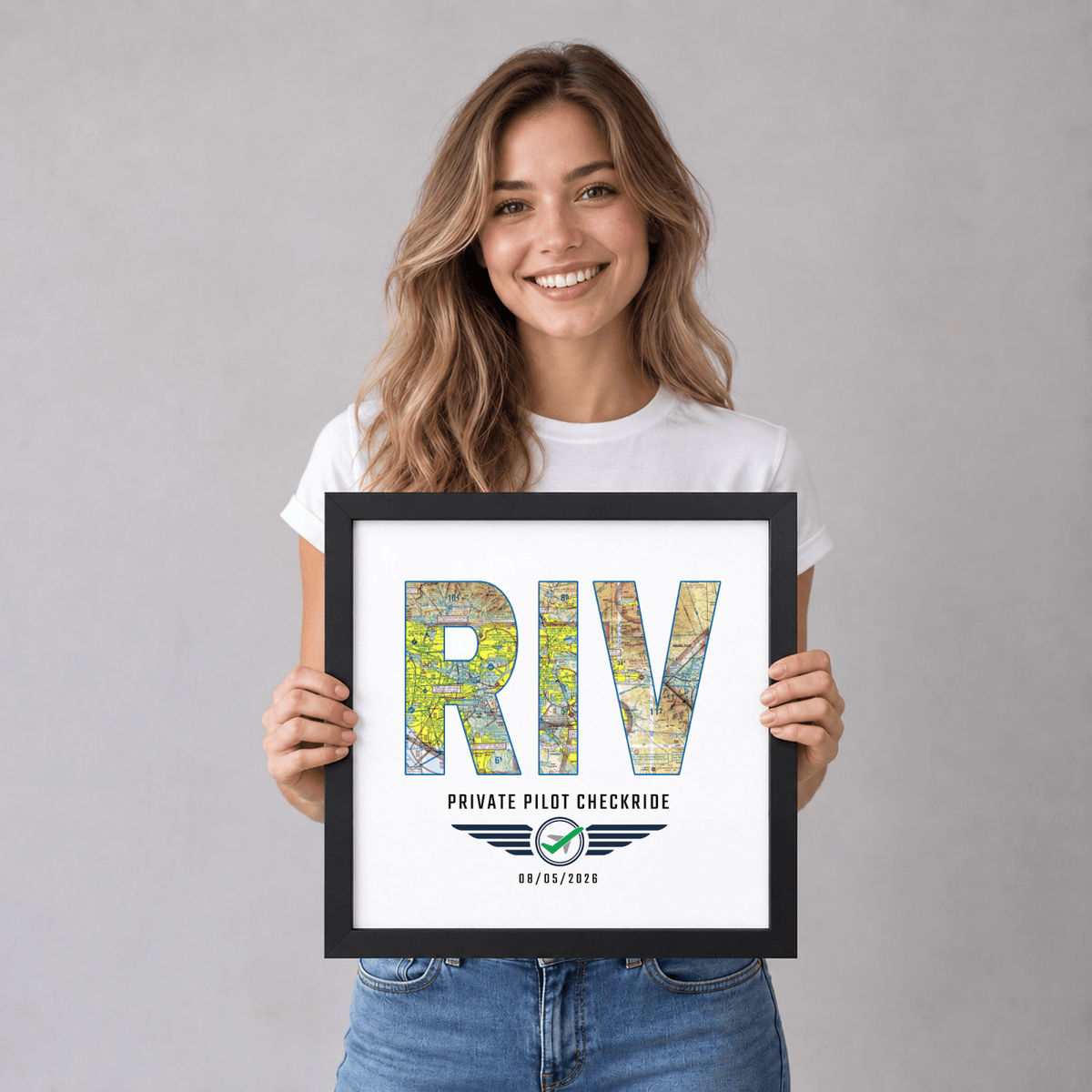 Woman holding a black-framed RIV airport code VFR chart print celebrating a private pilot checkride