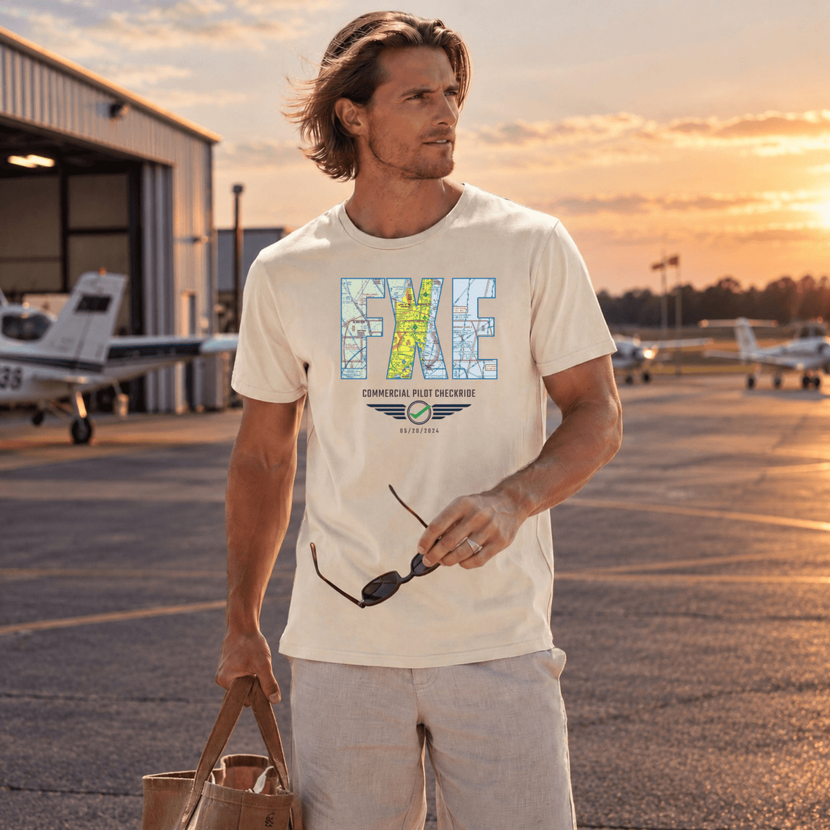 Man wearing a cream-colored FXE airport code VFR chart T-shirt outside an aircraft hangar