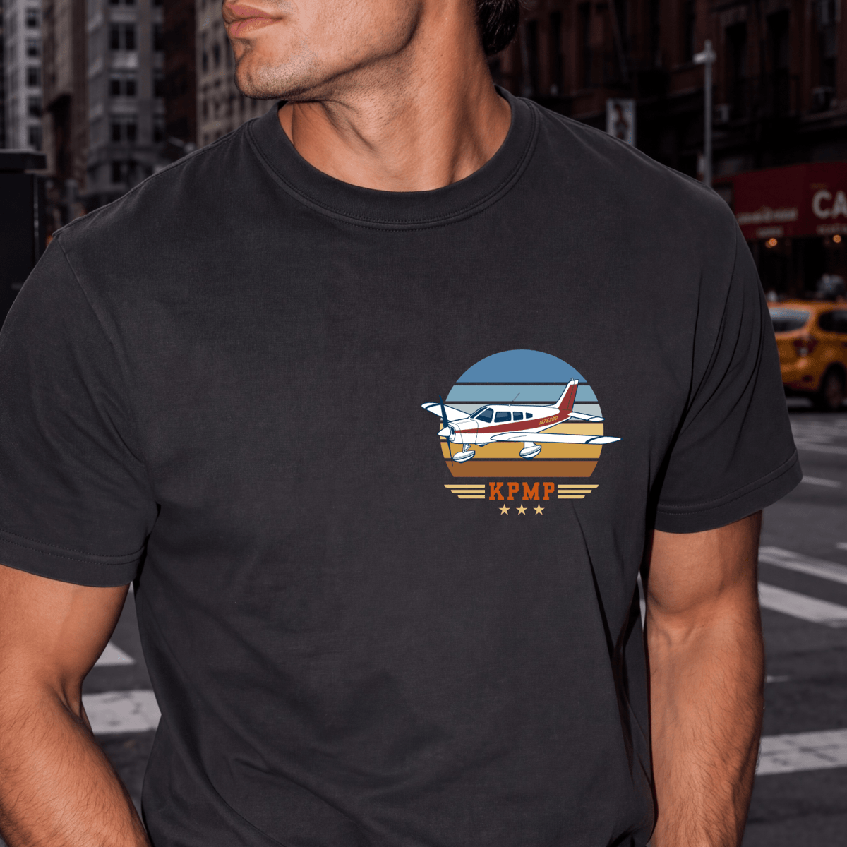 Man wearing a black Vintage Attitude T-shirt with a red-and-white airplane and KPMP airport code